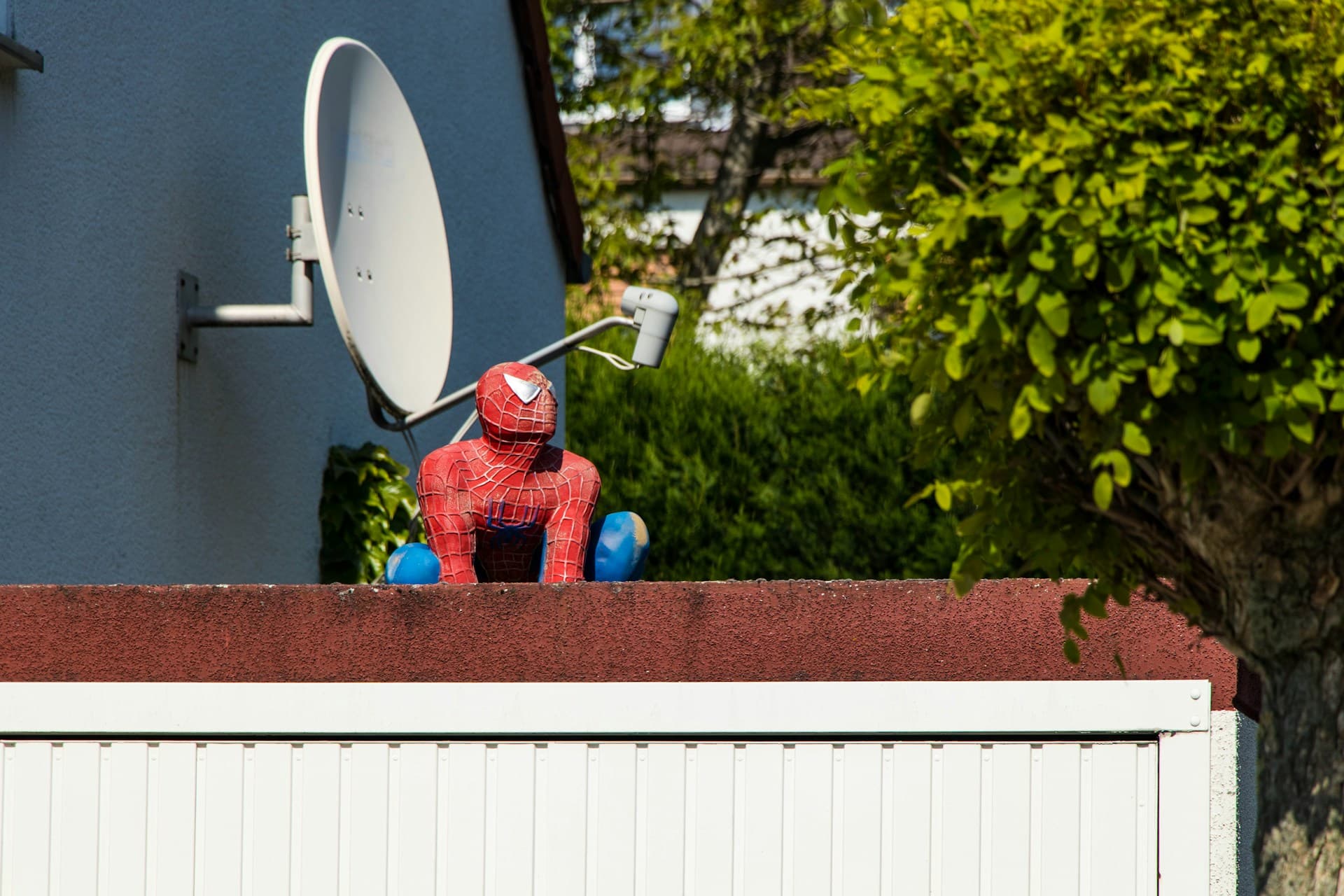 A man in a Spiderman costume perches atop a garage next to a satellite
